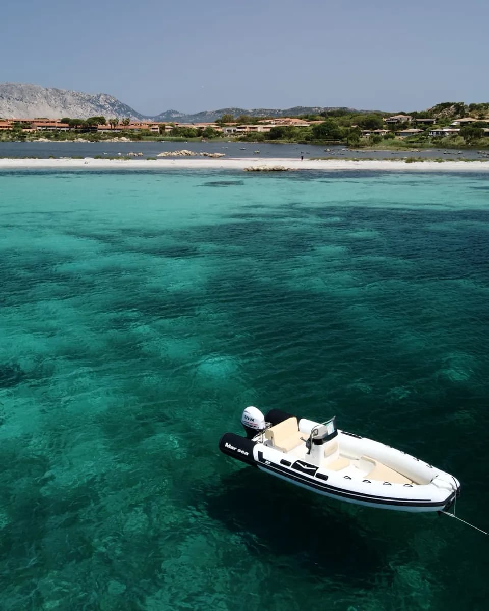 Un gommone ancorato nell'acqua turchese, con la spiaggia e l'isola sullo sfondo.